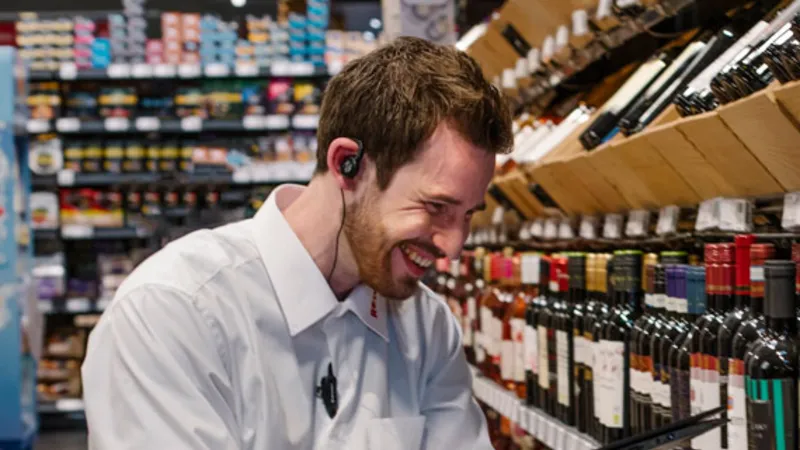 Ein REWE Student im Management-Traineeprogramm haelt ein Klemmbrett in der Hand vor dem Weinregal