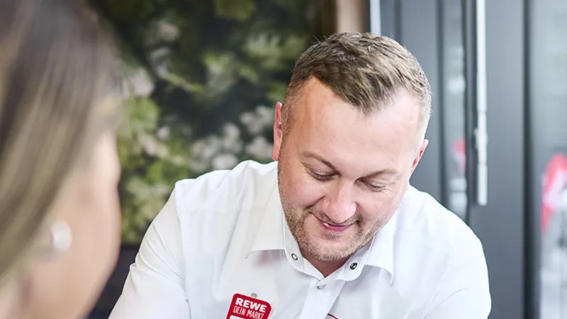 Ein REWE Mitarbeiter zeigt Produkte auf einem Handy