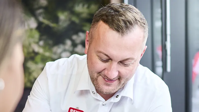 Ein REWE Mitarbeiter zeigt Produkte auf einem Handy