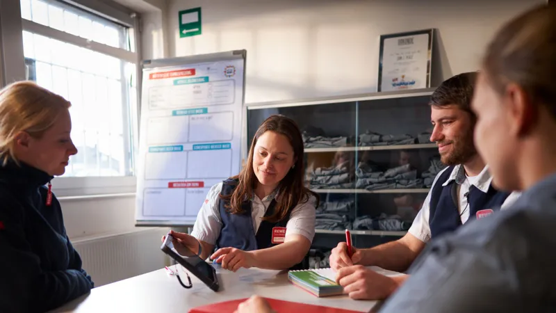 Ein selbstaendiger REWE Kaufmann kommuniziert offen mit Mitarbeitenden